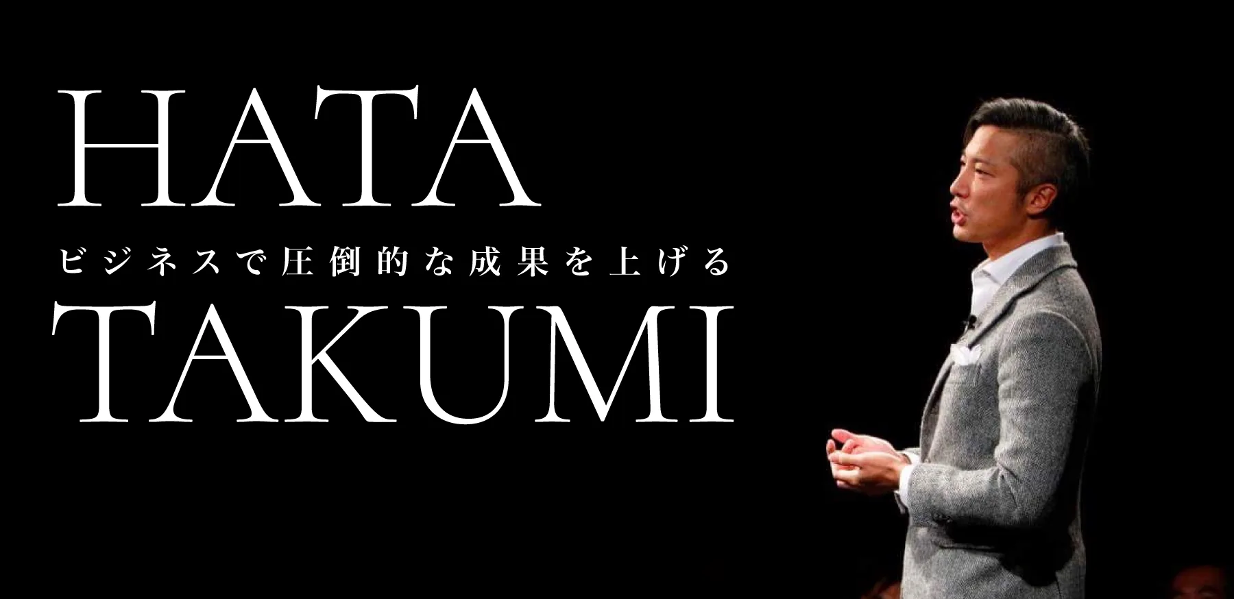 黒い舞台の上で聴衆に語りかける、グレーのジャケット姿の秦卓民
